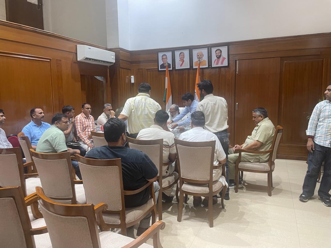 Wide view of the wood-paneled meeting room at the Haryana Secretariat, with officials seated and portraits of dignitaries on the wall