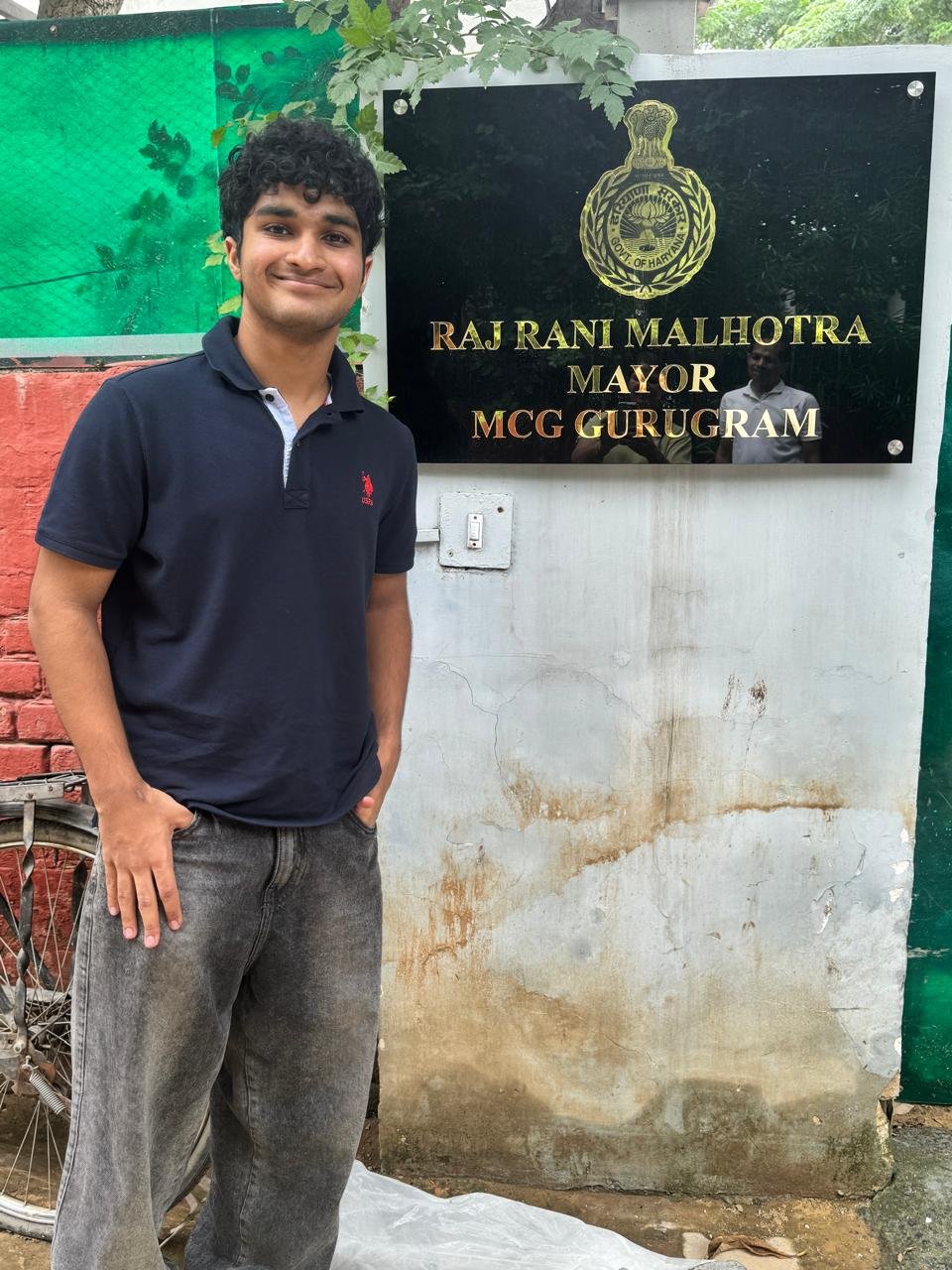 Standing outside the Mayor's office beside the sign reading Raj Rani Malhotra, Mayor, MCG Gurugram