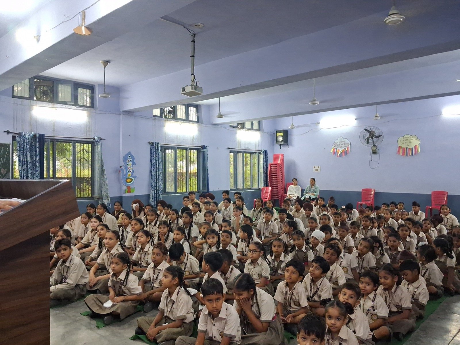 Addressing a full school assembly of students seated on the floor during a petition awareness session
